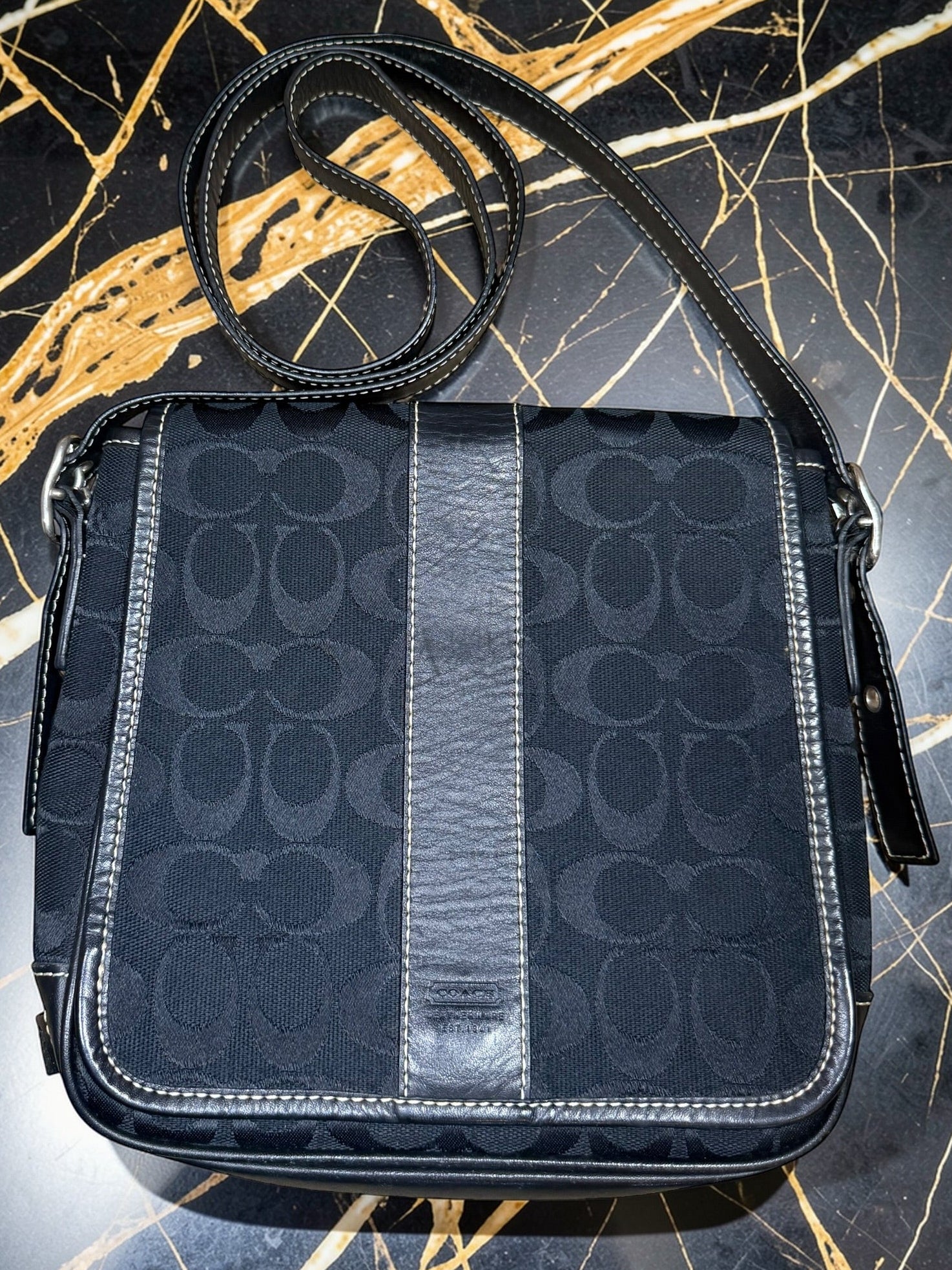Black handbag with a pattern on a black and gold marbled surface