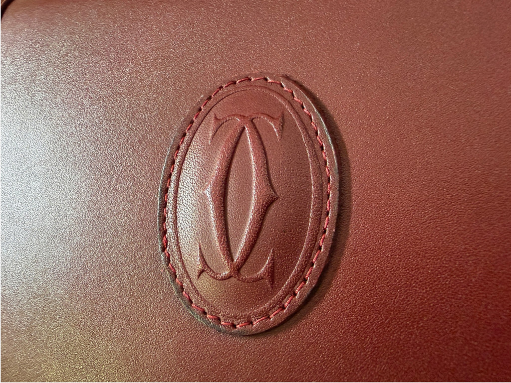 Close-up of embossed Cartier oval logo on burgundy leather